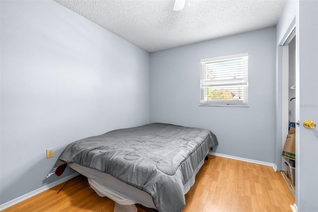 bedroom featuring baseboards, light wood-type flooring, and a textured ceiling