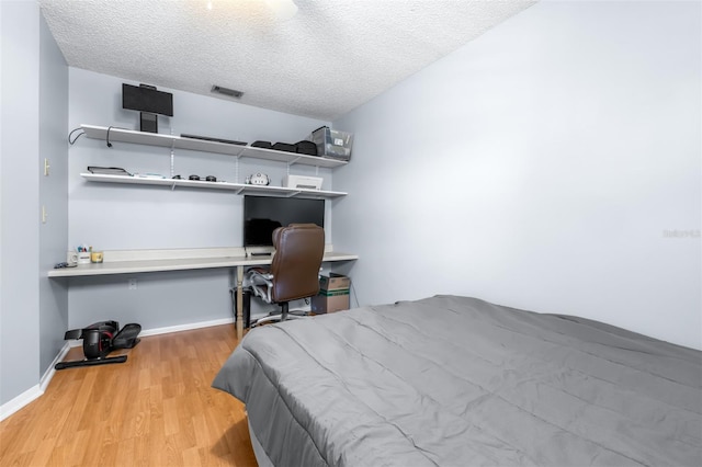 bedroom featuring baseboards, wood finished floors, visible vents, and a textured ceiling