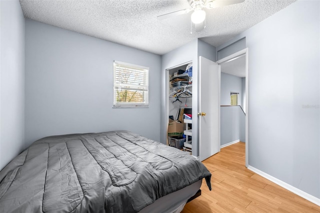 bedroom with baseboards, ceiling fan, light wood-style floors, a closet, and a textured ceiling