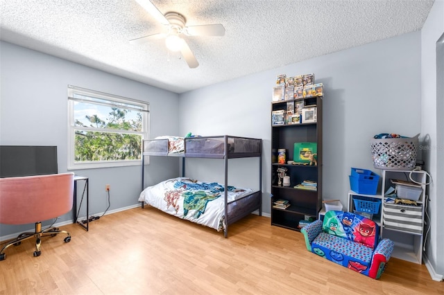 bedroom with ceiling fan, wood finished floors, baseboards, and a textured ceiling