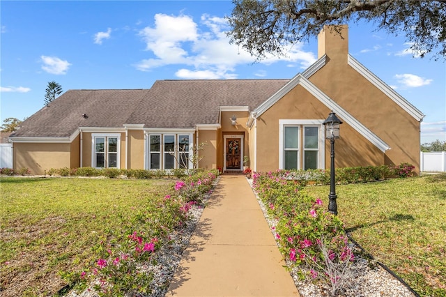 view of front of house featuring stucco siding, a chimney, a front yard, and fence