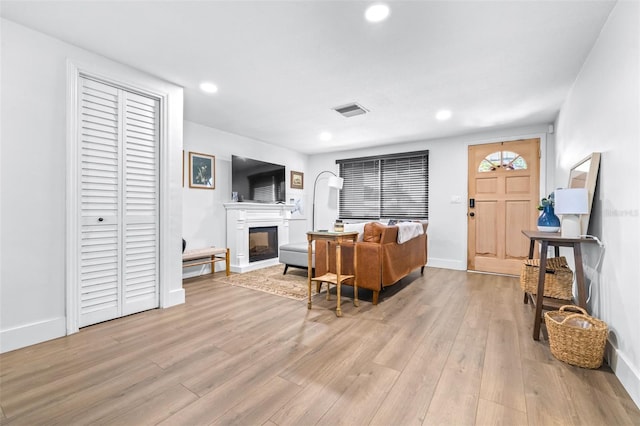 living area with a glass covered fireplace, light wood-style flooring, recessed lighting, and visible vents