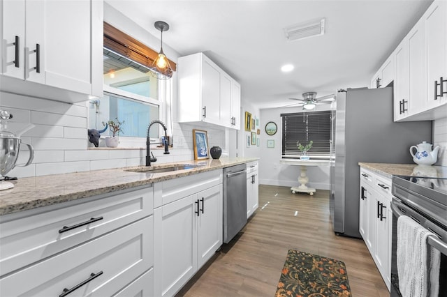 kitchen featuring a sink, backsplash, wood finished floors, appliances with stainless steel finishes, and white cabinets