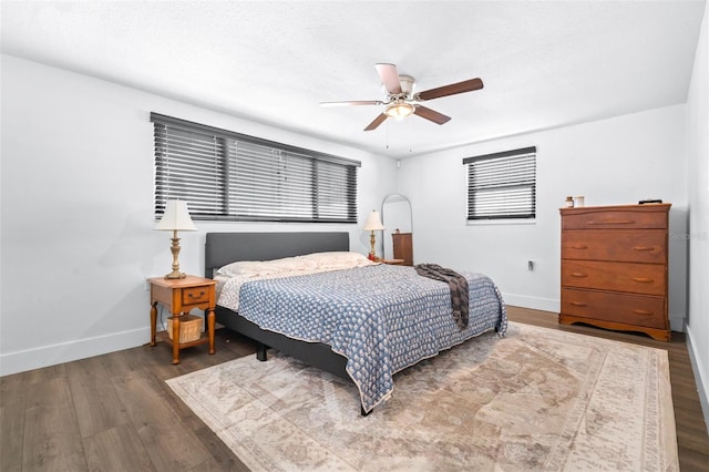 bedroom featuring ceiling fan, multiple windows, baseboards, and wood finished floors