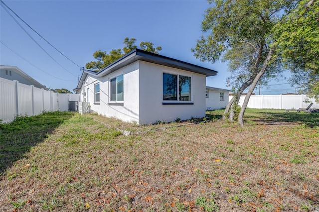 view of side of home featuring stucco siding, a yard, central AC, and fence