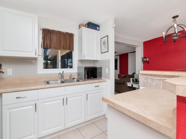 kitchen with light tile patterned floors, a sink, light countertops, white cabinetry, and stainless steel microwave