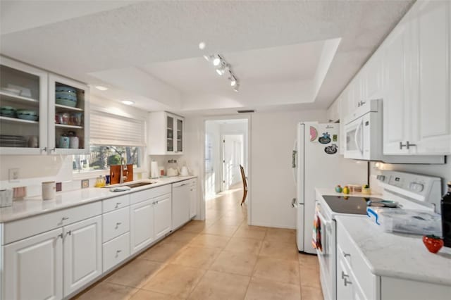 kitchen with white appliances, white cabinetry, a raised ceiling, and a sink