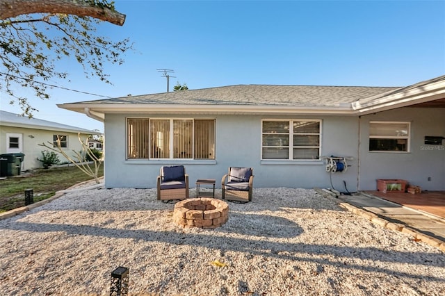 rear view of house with stucco siding, a fire pit, and roof with shingles