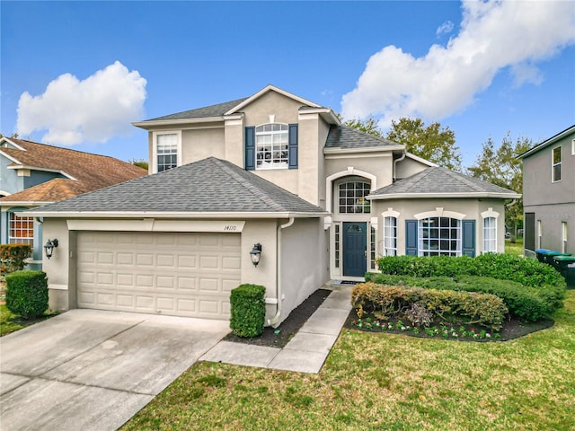 traditional-style house featuring a front yard, a shingled roof, stucco siding, concrete driveway, and a garage