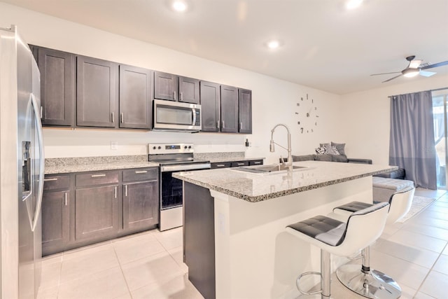 kitchen featuring a breakfast bar, a sink, light stone counters, appliances with stainless steel finishes, and light tile patterned floors