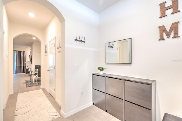 hallway with light tile patterned floors, baseboards, and arched walkways