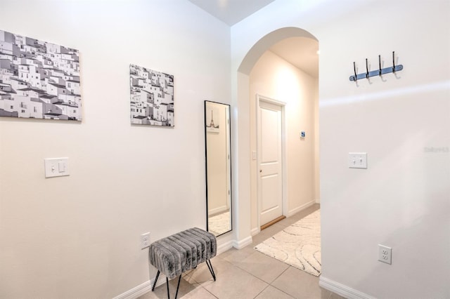 corridor with light tile patterned floors, baseboards, and arched walkways