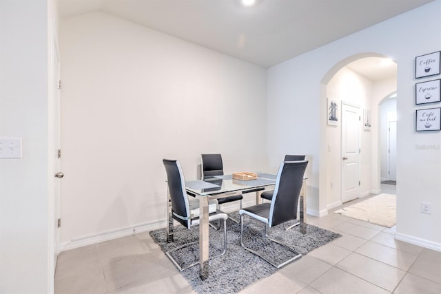 tiled dining space with lofted ceiling, baseboards, and arched walkways