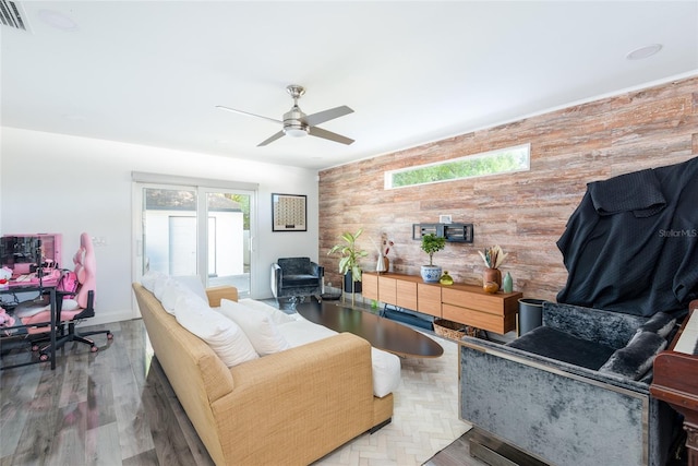 living room featuring wooden walls, a ceiling fan, wood finished floors, visible vents, and baseboards