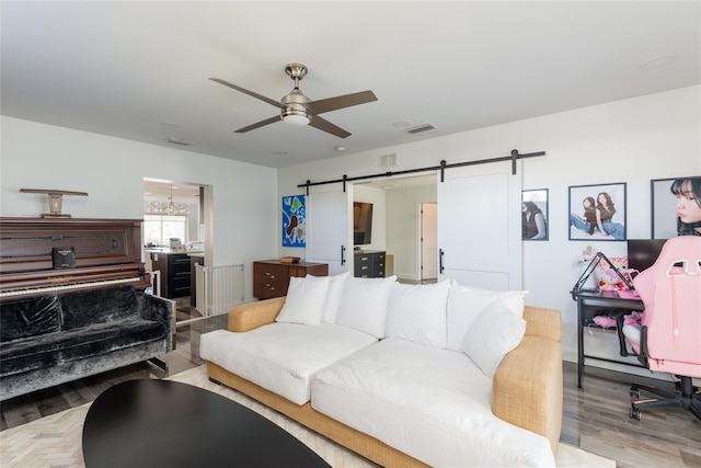 living room featuring visible vents, ceiling fan with notable chandelier, a barn door, and wood finished floors