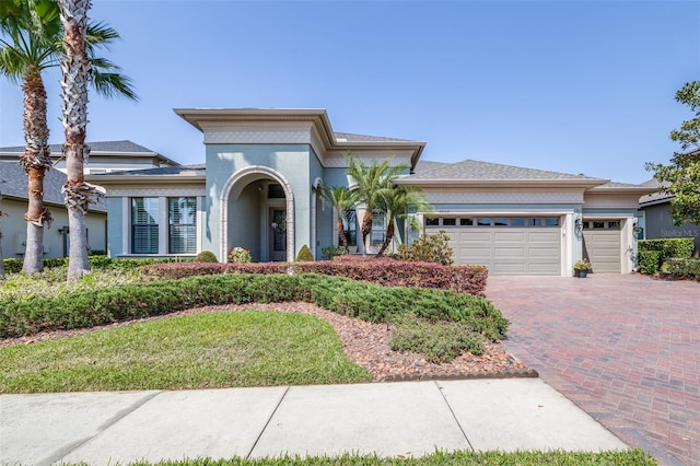 view of front of property with decorative driveway, an attached garage, and stucco siding