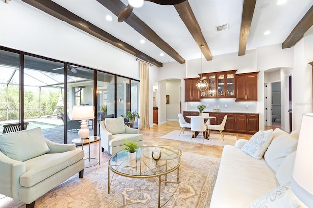 living area with beam ceiling, arched walkways, a sunroom, and ceiling fan