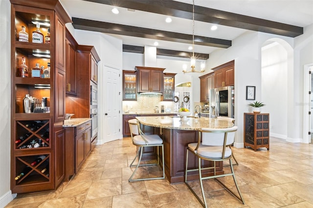 kitchen with tasteful backsplash, a breakfast bar, an island with sink, appliances with stainless steel finishes, and arched walkways