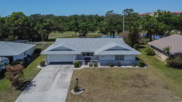view of front of property featuring a garage, concrete driveway, a front lawn, and roof with shingles