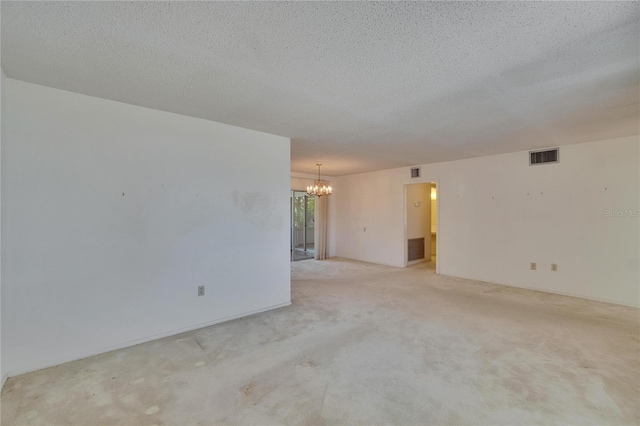 unfurnished room with a textured ceiling, visible vents, a notable chandelier, and light carpet