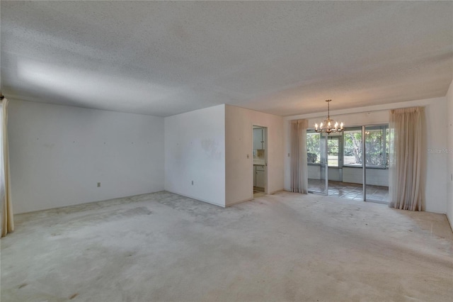 spare room featuring light carpet, a chandelier, and a textured ceiling