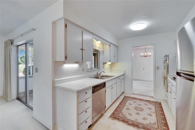 kitchen with a sink, light countertops, appliances with stainless steel finishes, and an inviting chandelier