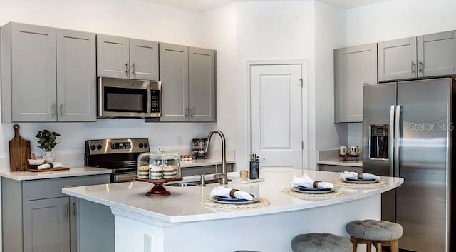 kitchen featuring a breakfast bar, a sink, gray cabinetry, light countertops, and appliances with stainless steel finishes