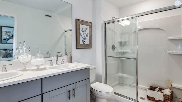 ensuite bathroom with double vanity, a shower stall, toilet, and a sink