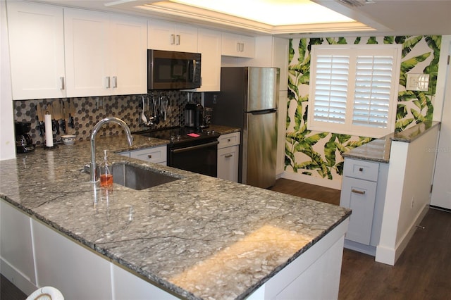 kitchen with a peninsula, freestanding refrigerator, black electric range oven, white cabinetry, and a sink