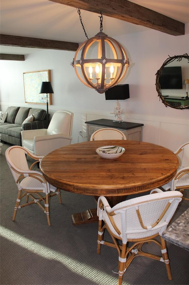 dining area with a wainscoted wall, beam ceiling, a notable chandelier, and carpet