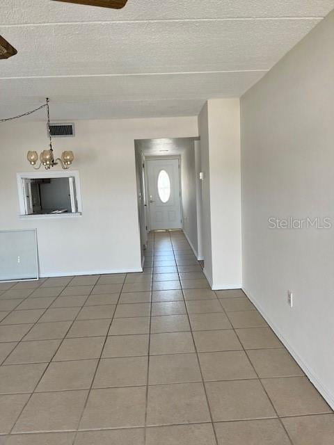 interior space with light tile patterned floors, visible vents, baseboards, a textured ceiling, and a chandelier