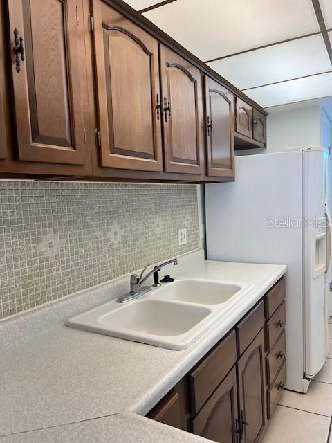 kitchen with light tile patterned flooring, backsplash, light countertops, and a sink