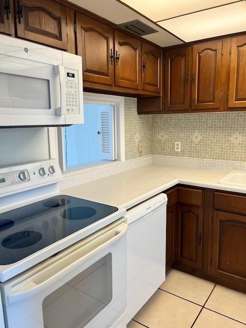 kitchen featuring light tile patterned floors, decorative backsplash, white appliances, and light countertops