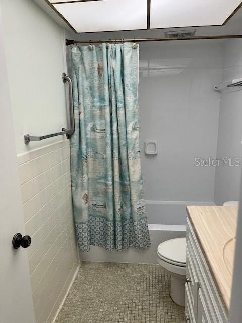 bathroom featuring shower / bath combo with shower curtain, toilet, tile walls, tile patterned flooring, and vanity