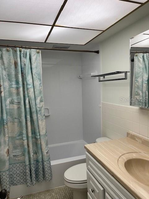 bathroom with toilet, vanity, tile patterned floors, tile walls, and shower / bathtub combination with curtain