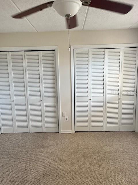 unfurnished bedroom with a textured ceiling, a ceiling fan, multiple closets, and carpet floors