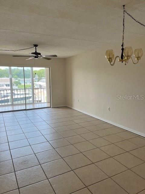 empty room with light tile patterned floors, ceiling fan with notable chandelier, and baseboards