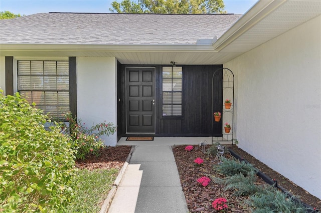 doorway to property with stucco siding and roof with shingles