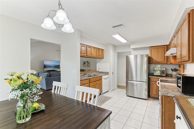 kitchen featuring visible vents, under cabinet range hood, appliances with stainless steel finishes, brown cabinetry, and a sink