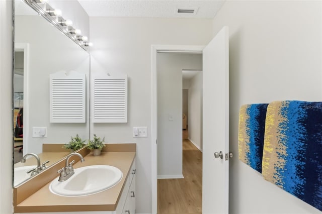 bathroom with vanity, wood finished floors, visible vents, baseboards, and a textured ceiling