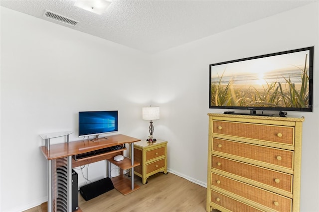 home office with visible vents, baseboards, light wood-style floors, and a textured ceiling