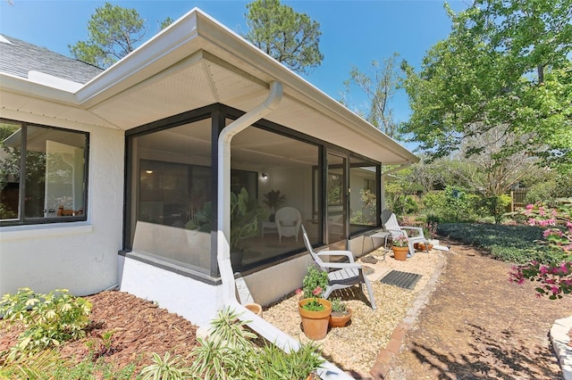 rear view of property featuring stucco siding, a sunroom, and roof with shingles