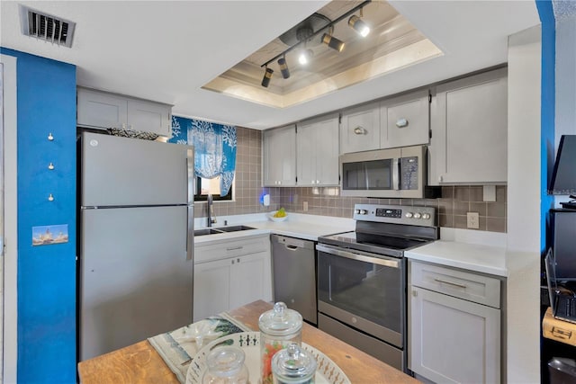 kitchen featuring visible vents, a sink, a tray ceiling, backsplash, and stainless steel appliances