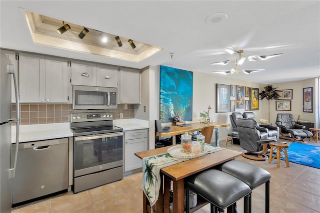 kitchen with tasteful backsplash, light countertops, a tray ceiling, light tile patterned floors, and stainless steel appliances