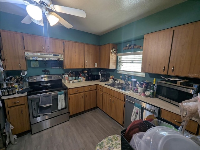 kitchen with under cabinet range hood, light countertops, appliances with stainless steel finishes, and a sink