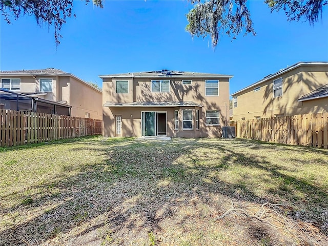 back of house with stucco siding, a lawn, central AC, and a fenced backyard