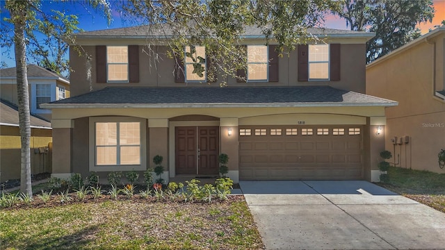 traditional-style house featuring stucco siding, an attached garage, roof with shingles, and driveway