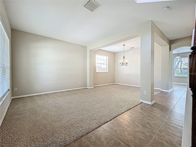 carpeted spare room featuring tile patterned floors, visible vents, arched walkways, baseboards, and a chandelier