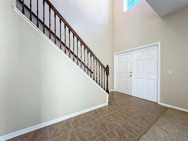 foyer with dark tile patterned floors, baseboards, stairs, and a towering ceiling