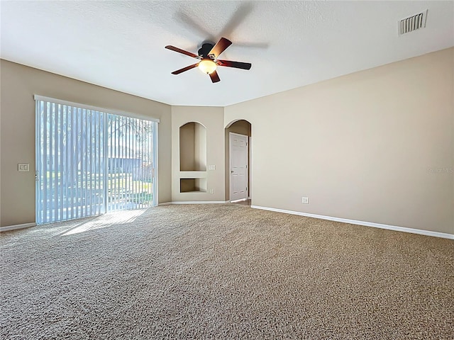 carpeted spare room featuring baseboards, arched walkways, visible vents, and a textured ceiling